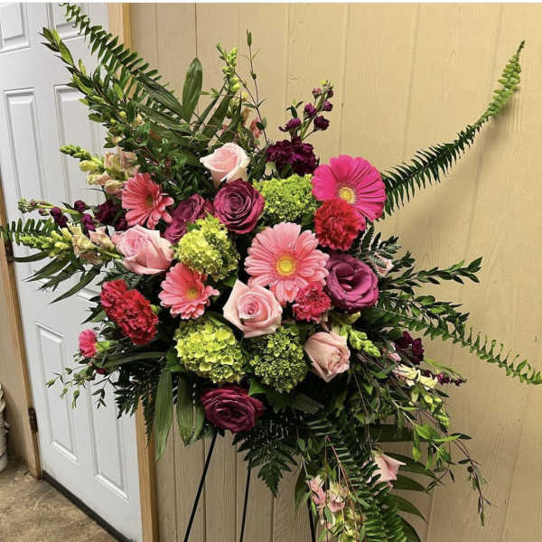 Standing floral spray with pink and burgundy blooms on a black easel