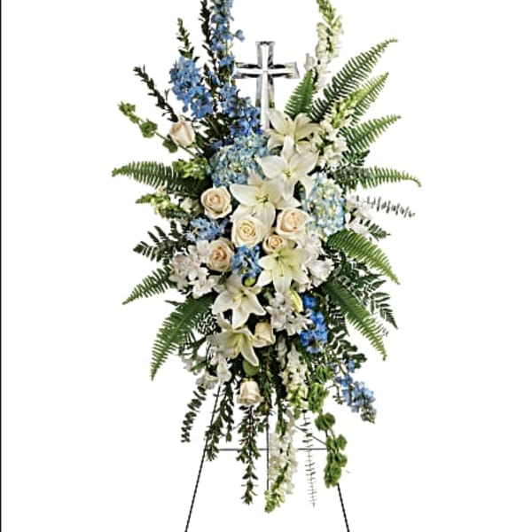 Standing floral spray with white lilies, blue flowers, and a cross