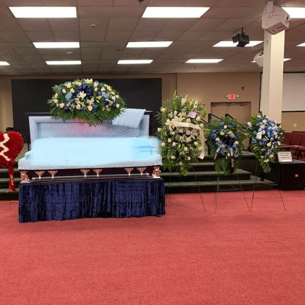 Casket surrounded by blue and white funeral flower sprays