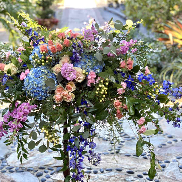 Large colorful floral arrangement with roses, hydrangeas, and hanging blooms