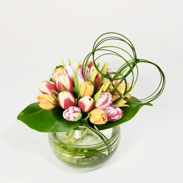 Tulip arrangement in a round glass vase with decorative loops