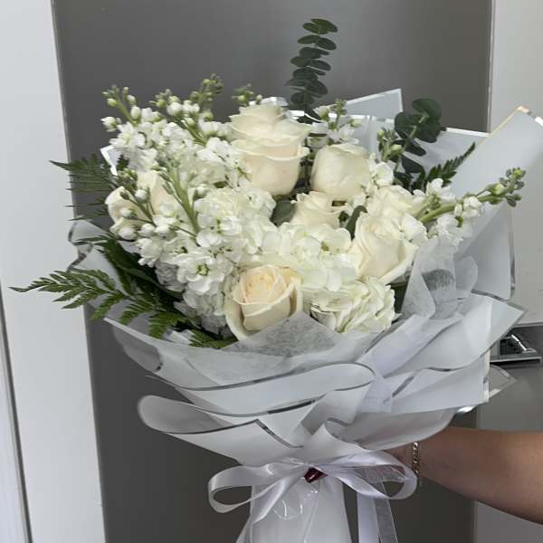 Bouquet of white roses and white filler flowers wrapped in white paper