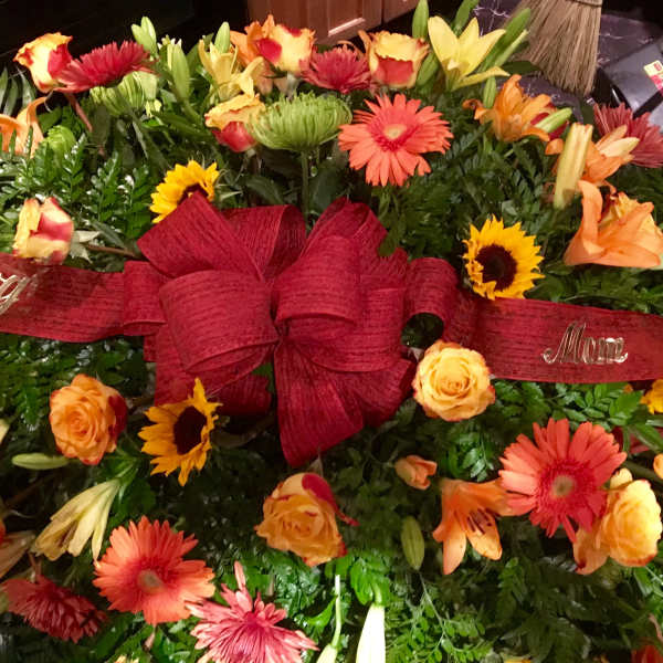Large floral spray with red ribbon and mixed orange, yellow, and pink flowers