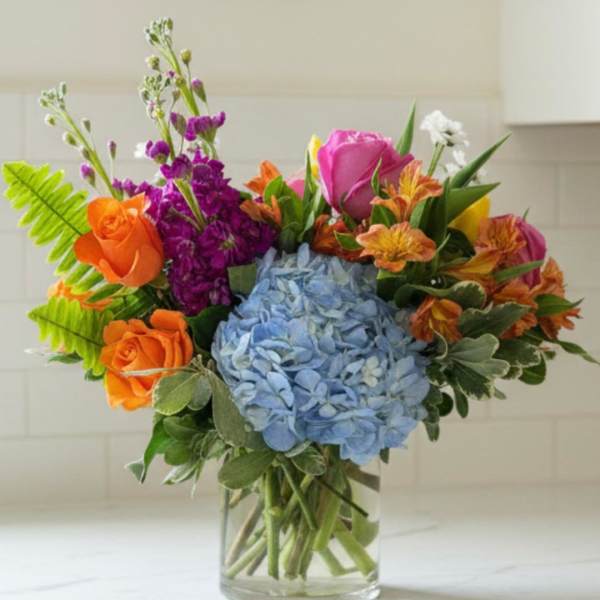 Colorful bouquet with blue hydrangea, orange and pink roses in a glass vase