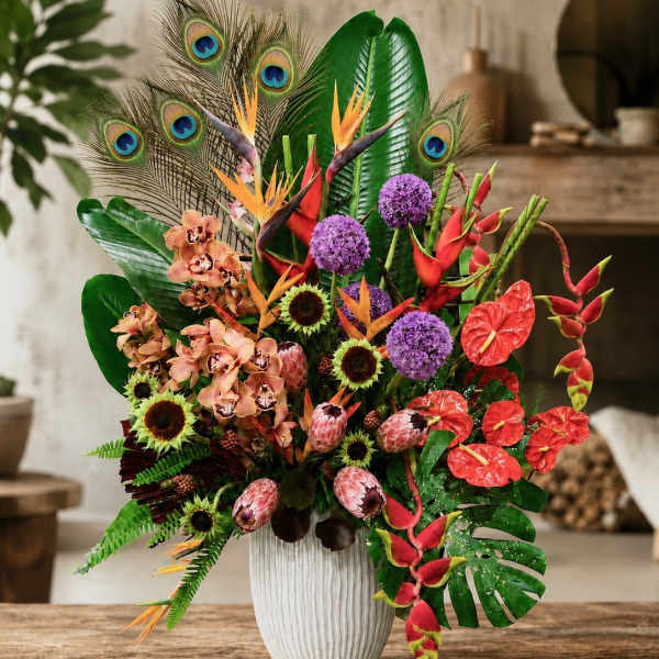Tropical bouquet in a white vase with orchids, birds of paradise, and peacock feathers