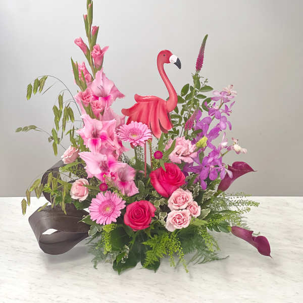 Pink floral arrangement with roses, orchids, and a flamingo decoration