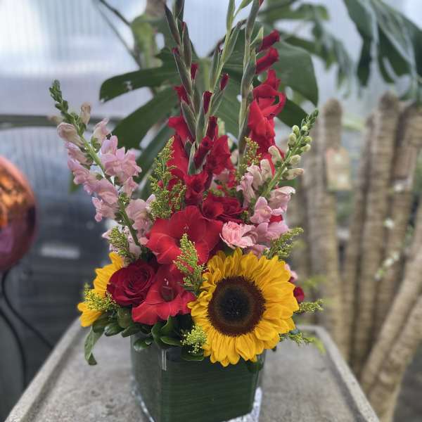 Tall mixed bouquet with sunflowers, red gladiolus, and pink snapdragons in a glass vase