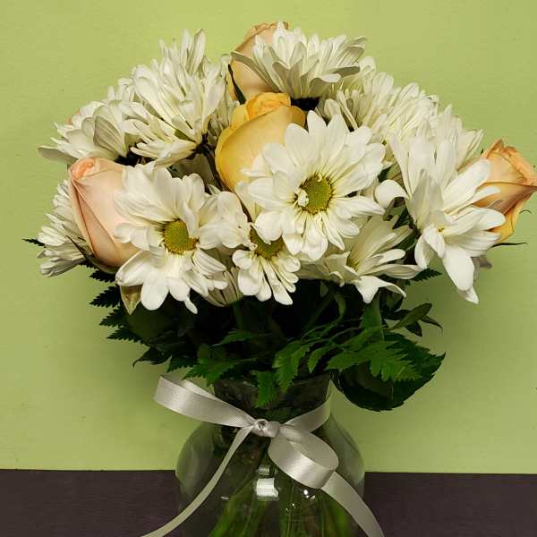 White daisies and pale peach roses in a glass vase with a ribbon
