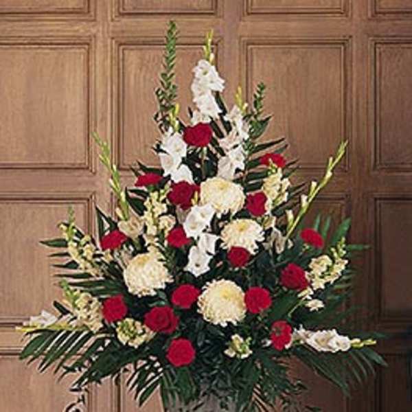 Tall arrangement of red roses, white gladiolus, and cream flowers in an urn-style vase.
