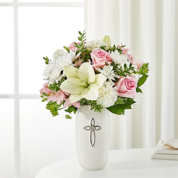 Pink roses and white lilies in a white vase with a cross emblem