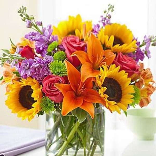 Bouquet of sunflowers, orange lilies, pink roses, and purple flowers in a glass vase