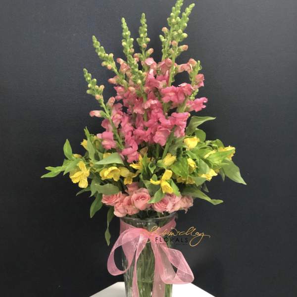 Pink and yellow flowers in a clear glass vase with a pink ribbon