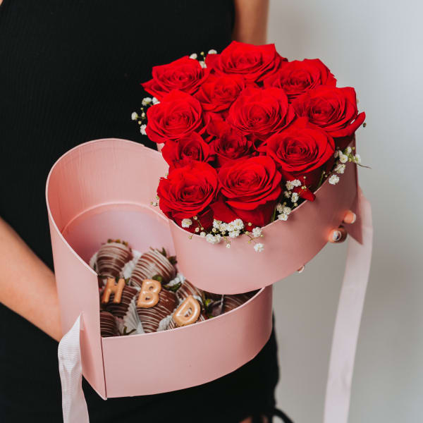 Woman holding a pink heart-shaped box with red roses and chocolate-covered strawberries