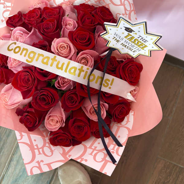 Bouquet of red and pink roses wrapped in pink paper with a congratulations ribbon