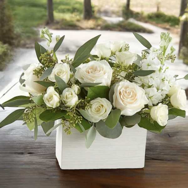 White roses arranged in a white rectangular box with greenery