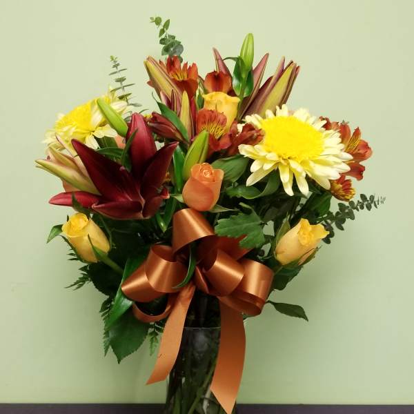 Mixed bouquet of lilies, roses, and daisies in a glass vase with a ribbon