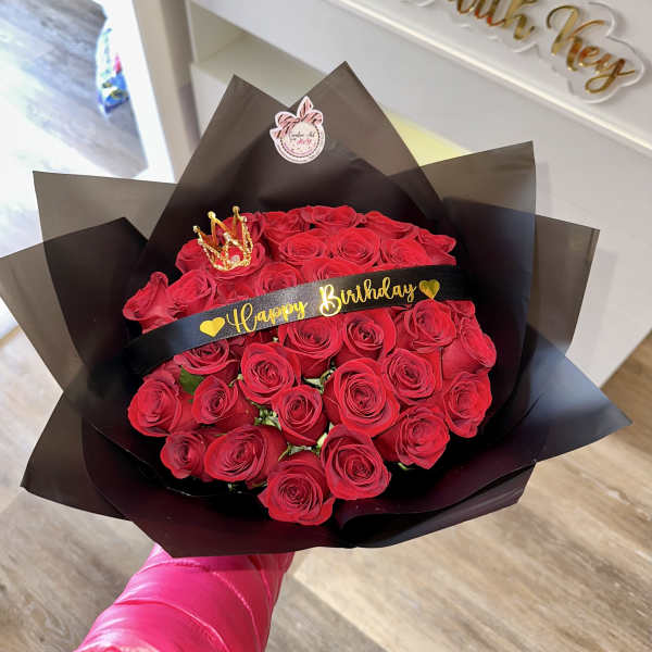 Bouquet of red roses wrapped in black paper with a birthday ribbon and crown topper