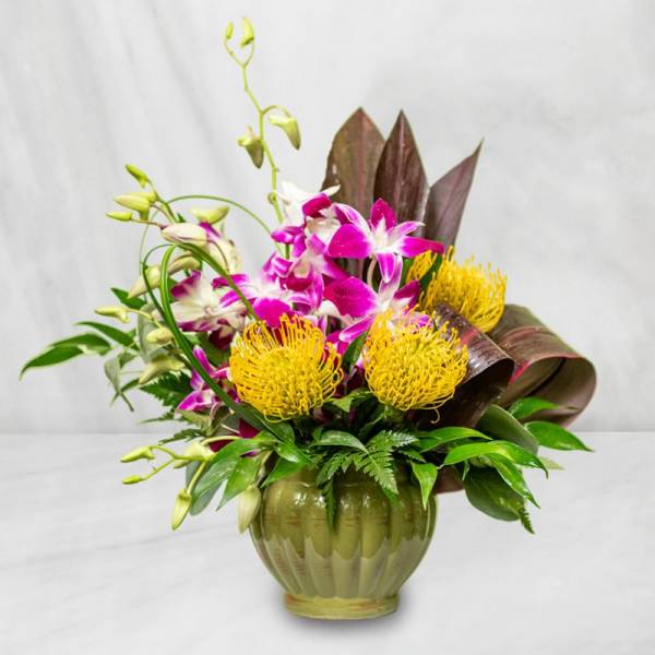Tropical floral arrangement in a green glass vase with purple orchids and yellow blooms