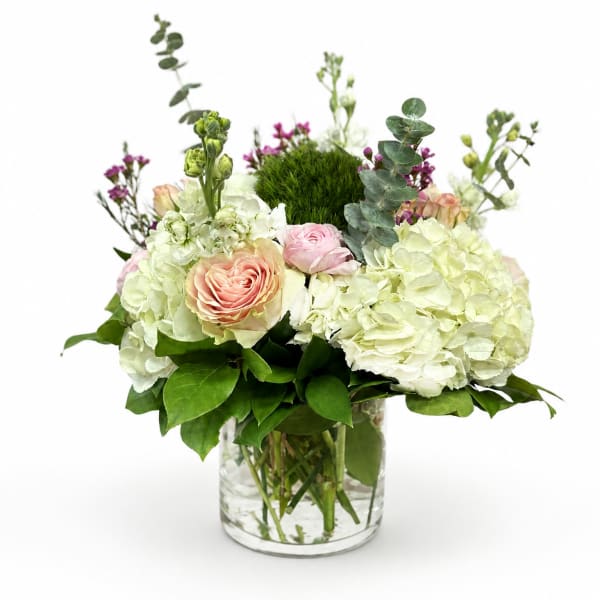 White hydrangeas and blush roses in a clear glass vase