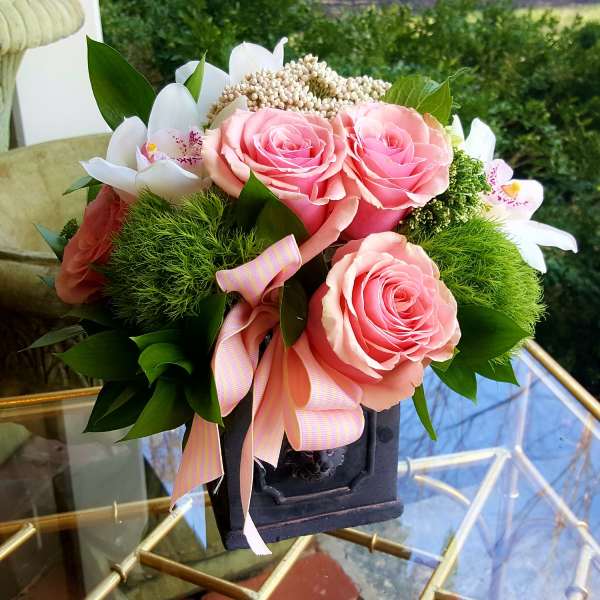Pink roses and white orchids arranged in a dark vase with a striped ribbon