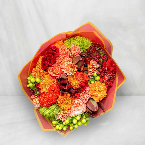 Bright mixed bouquet with orange, red, and pink flowers wrapped in paper