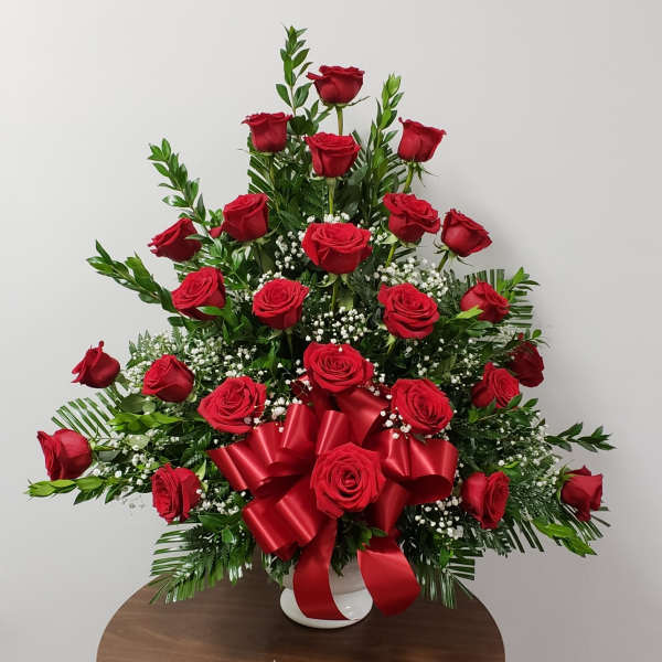Red roses arranged in a white vase with a red ribbon