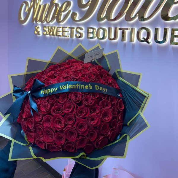 Large bouquet of red roses wrapped in dark paper with a Valentine ribbon