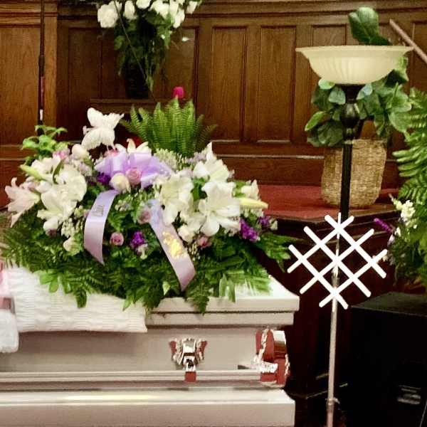 White casket surrounded by purple and white funeral flower sprays