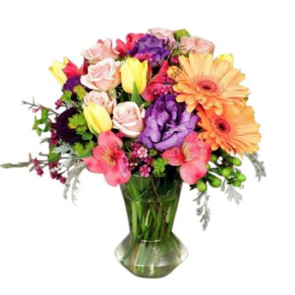 Colorful mixed bouquet in a clear glass vase with gerbera daisies, roses, and tulips
