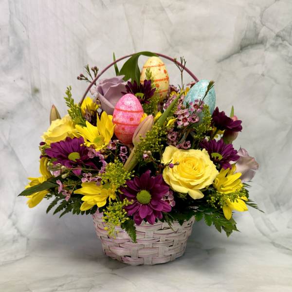 Basket arrangement of yellow and purple flowers with decorative Easter eggs