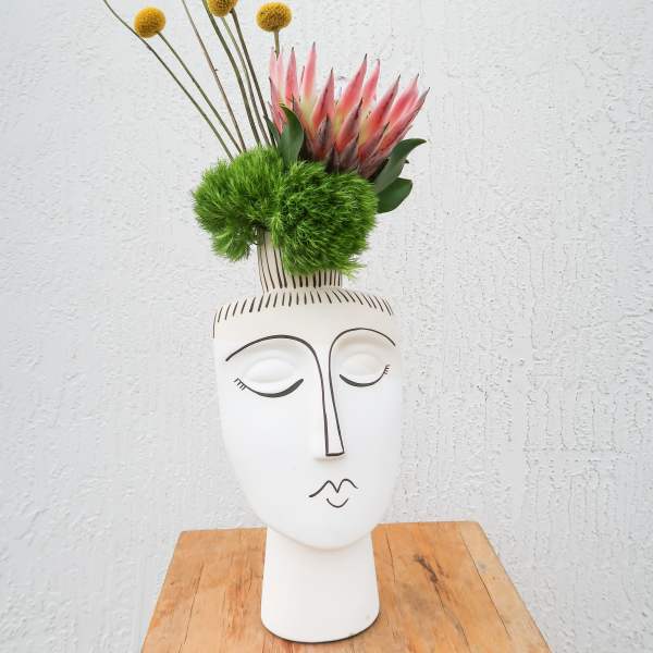 Modern floral arrangement in a white face vase with pink protea and yellow globe flowers
