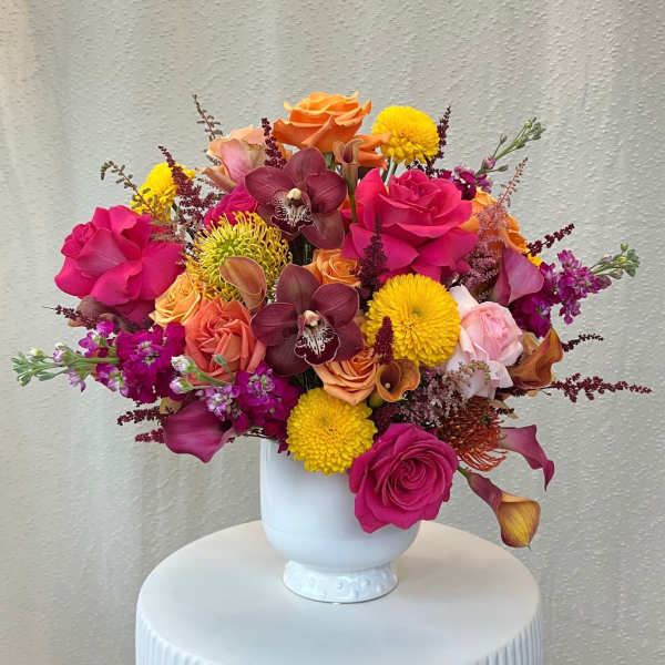 Bright mixed bouquet in a white vase with roses, orchids, and mums