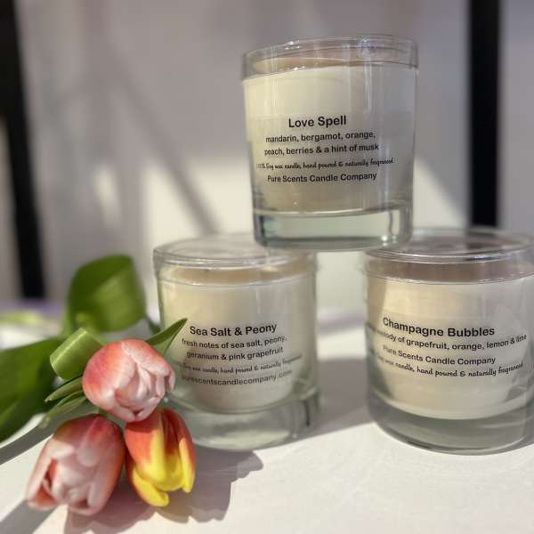 Set of three scented glass candles with printed labels, styled beside orange and yellow tulips.