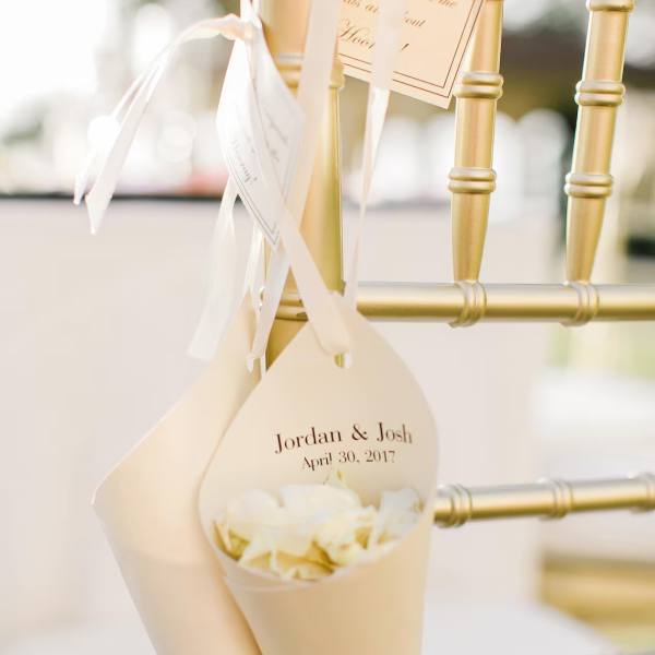 Cream wedding favor cones tied to a gold chair with white ribbon