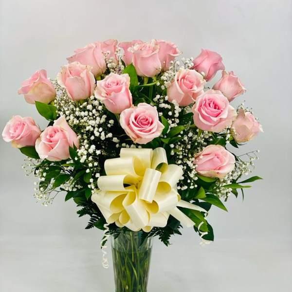 Pink rose bouquet in a clear glass vase with a cream ribbon bow