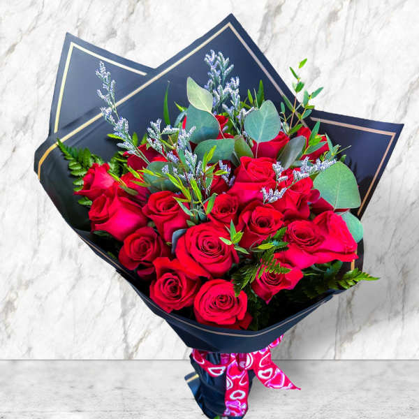 Bouquet of red roses wrapped in dark paper with a pink ribbon