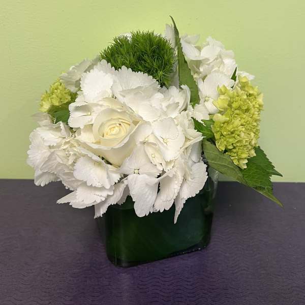 White hydrangeas and a cream rose in a dark green vase