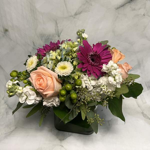 Mixed bouquet with peach roses, magenta daisies, and white blooms in a dark vase