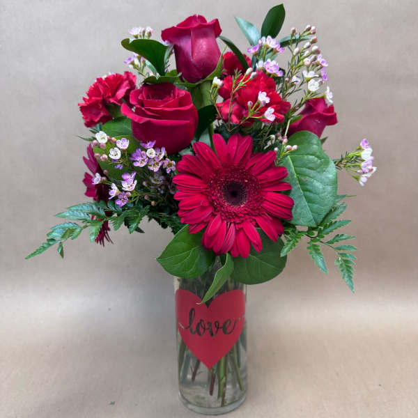 Red roses and a gerbera daisy in a glass vase with a heart label
