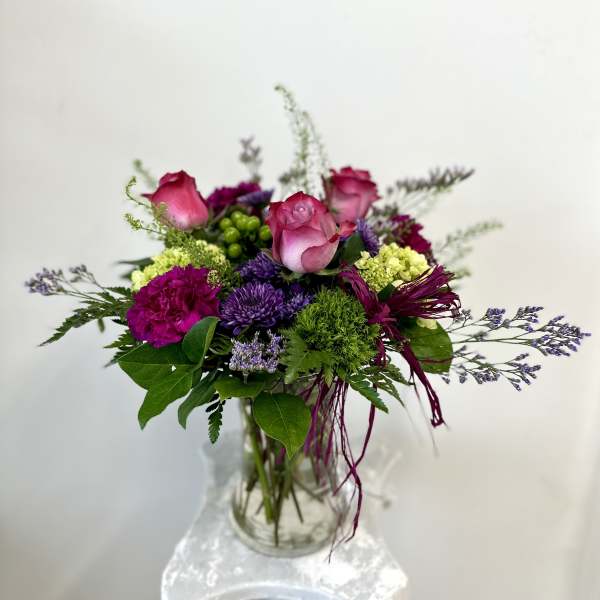 Pink roses and purple flowers in a clear glass vase