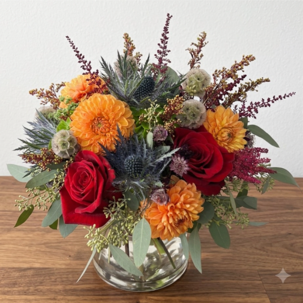 Bouquet of red roses and orange dahlias in a clear glass vase