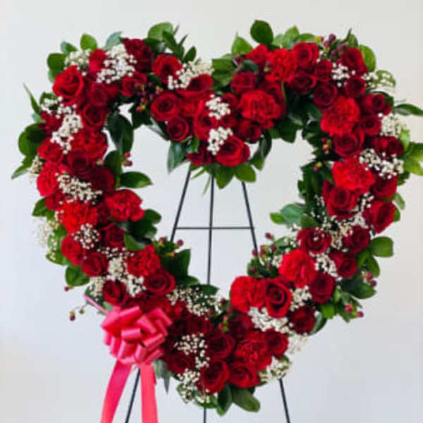 Heart-shaped red rose wreath on a stand with a pink ribbon bow