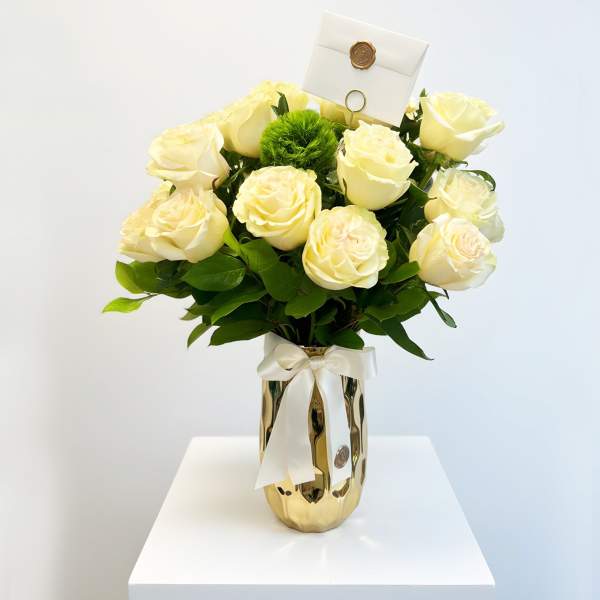 White roses in a gold vase with a ribbon and card holder.