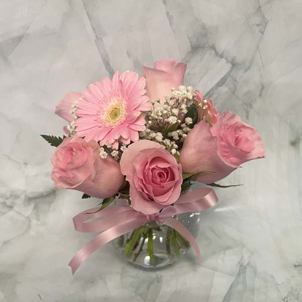 Pink roses and a gerbera daisy in a glass vase with a pink ribbon