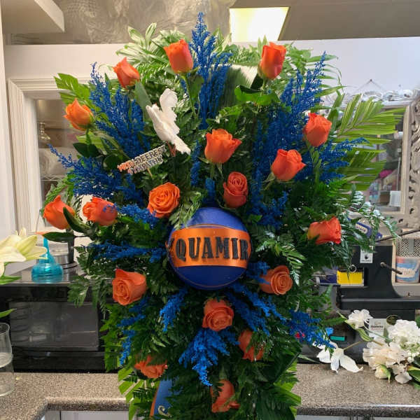 Large orange rose funeral spray with blue accents and a memorial ribbon