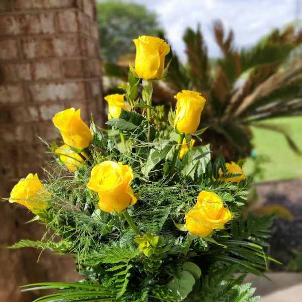 Yellow roses arranged in a glass vase with fern foliage