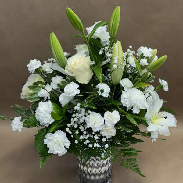 White floral arrangement with lilies, roses, and carnations in a patterned vase