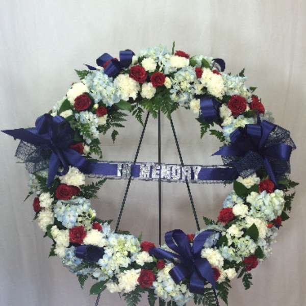 Heart-shaped funeral wreath with red, white, and blue flowers on an easel