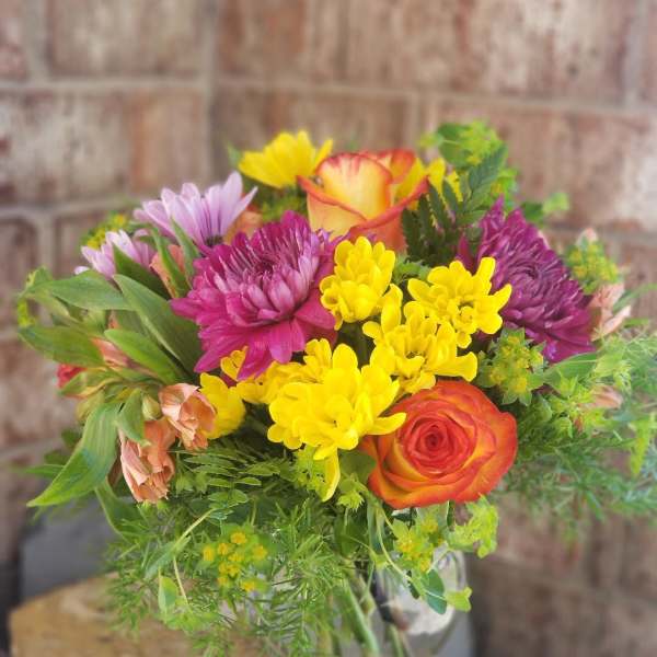 Mixed bouquet of yellow, purple, and orange flowers in a glass vase