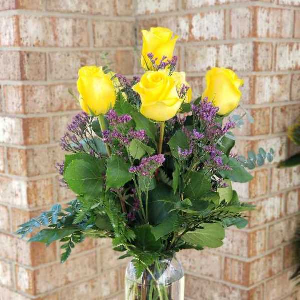 Yellow roses with purple filler in a clear glass vase